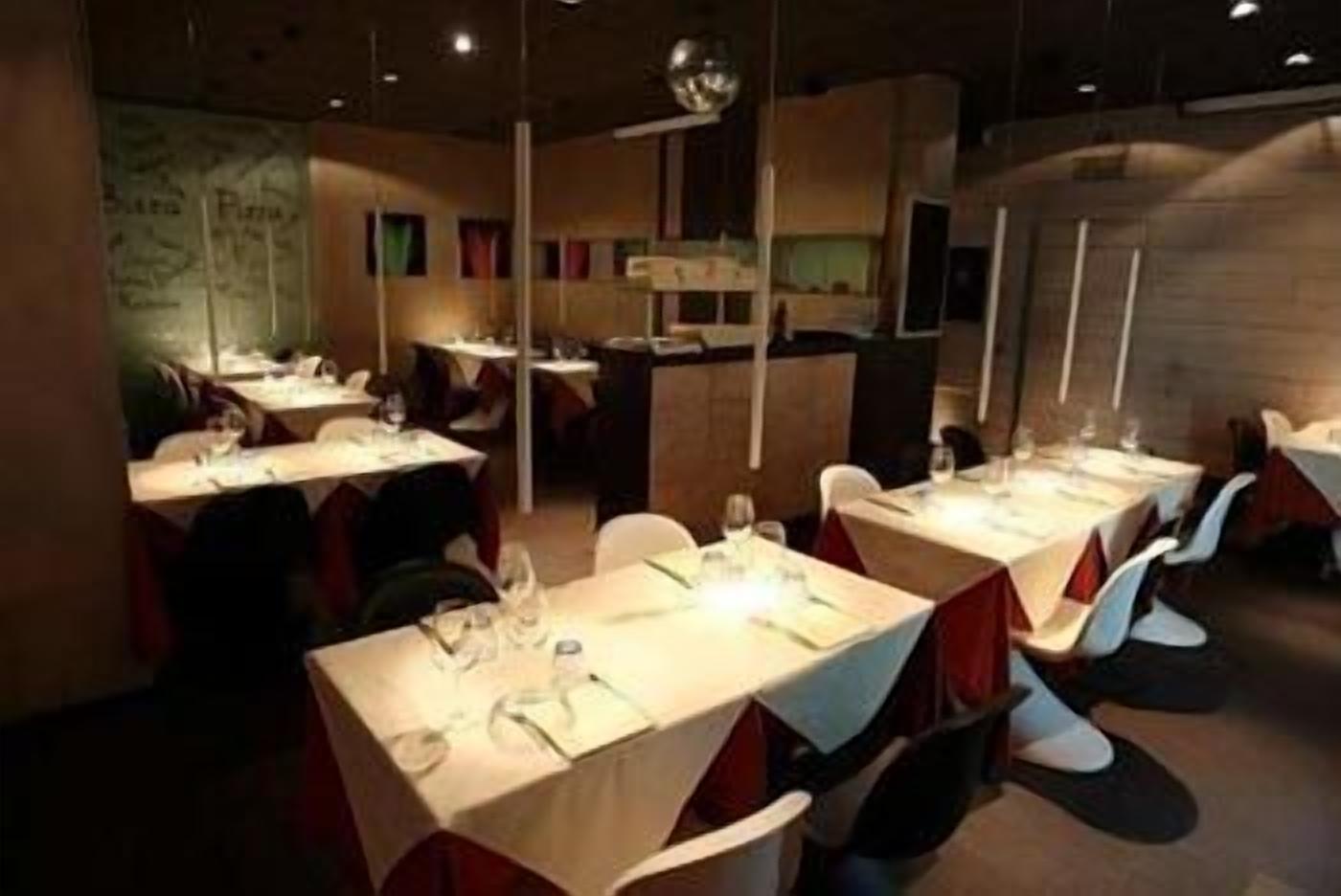 Ein Restaurant mit mehreren Tischen, gedeckt mit Besteck und Gläsern, und einer Bar im Hintergrund.
