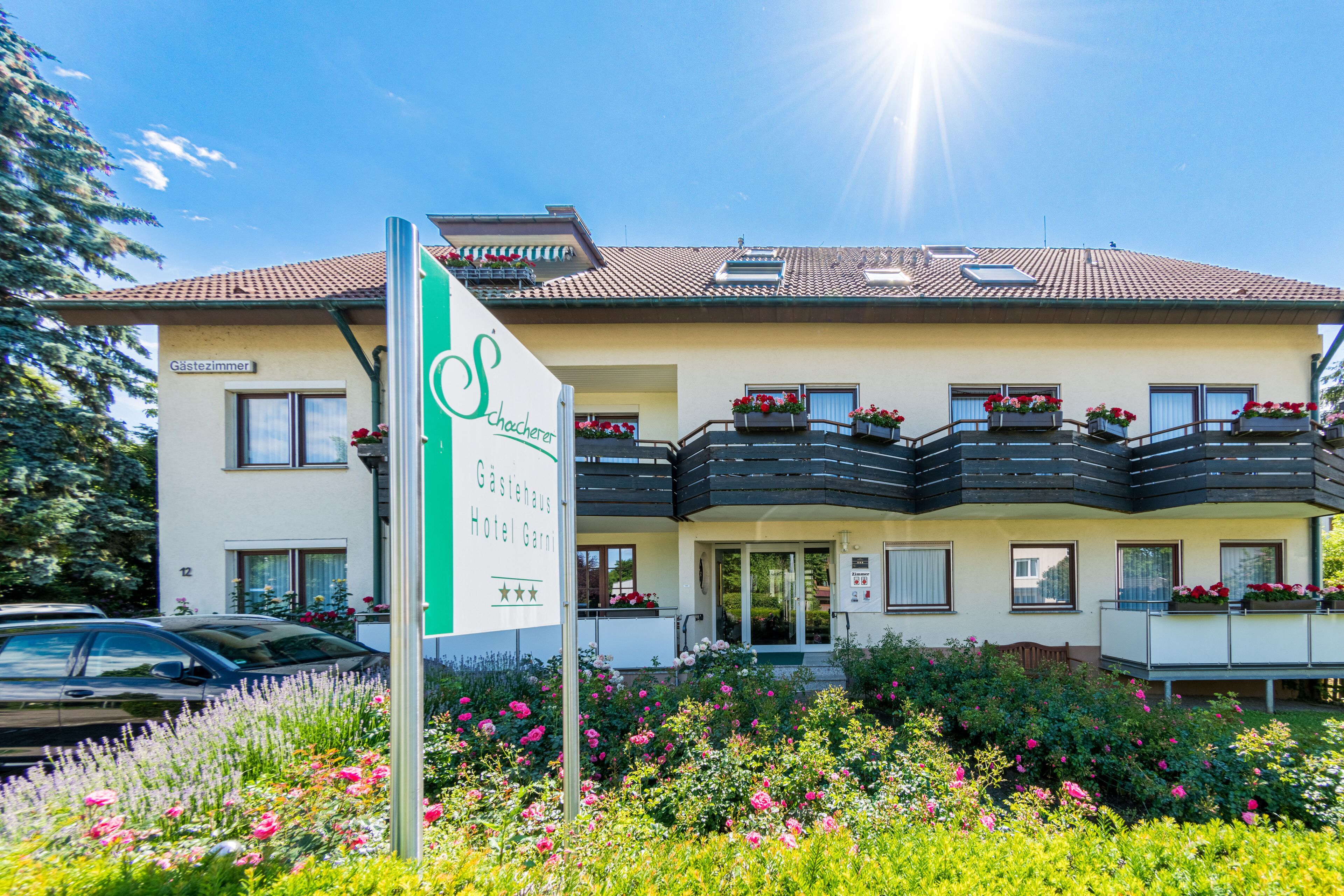 Ein Hotel mit einem Schild, das es als 'Gästehaus Hotel Garn' kennzeichnet. Es verfügt über einen Balkon mit Blumenkästen und einen gepflegten Garten davor.