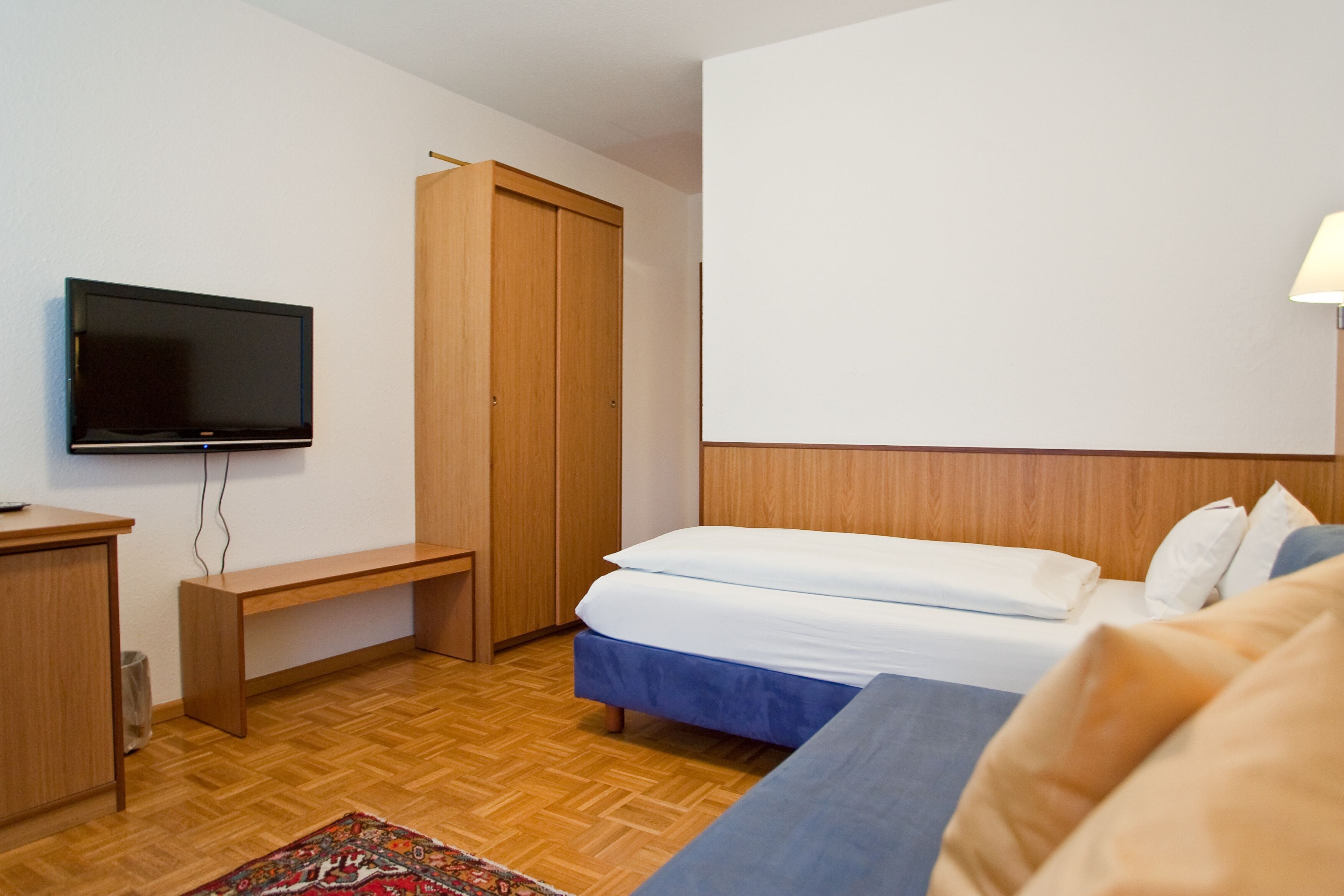 A hotel room with a bed, a TV, a wooden wardrobe, and a desk.