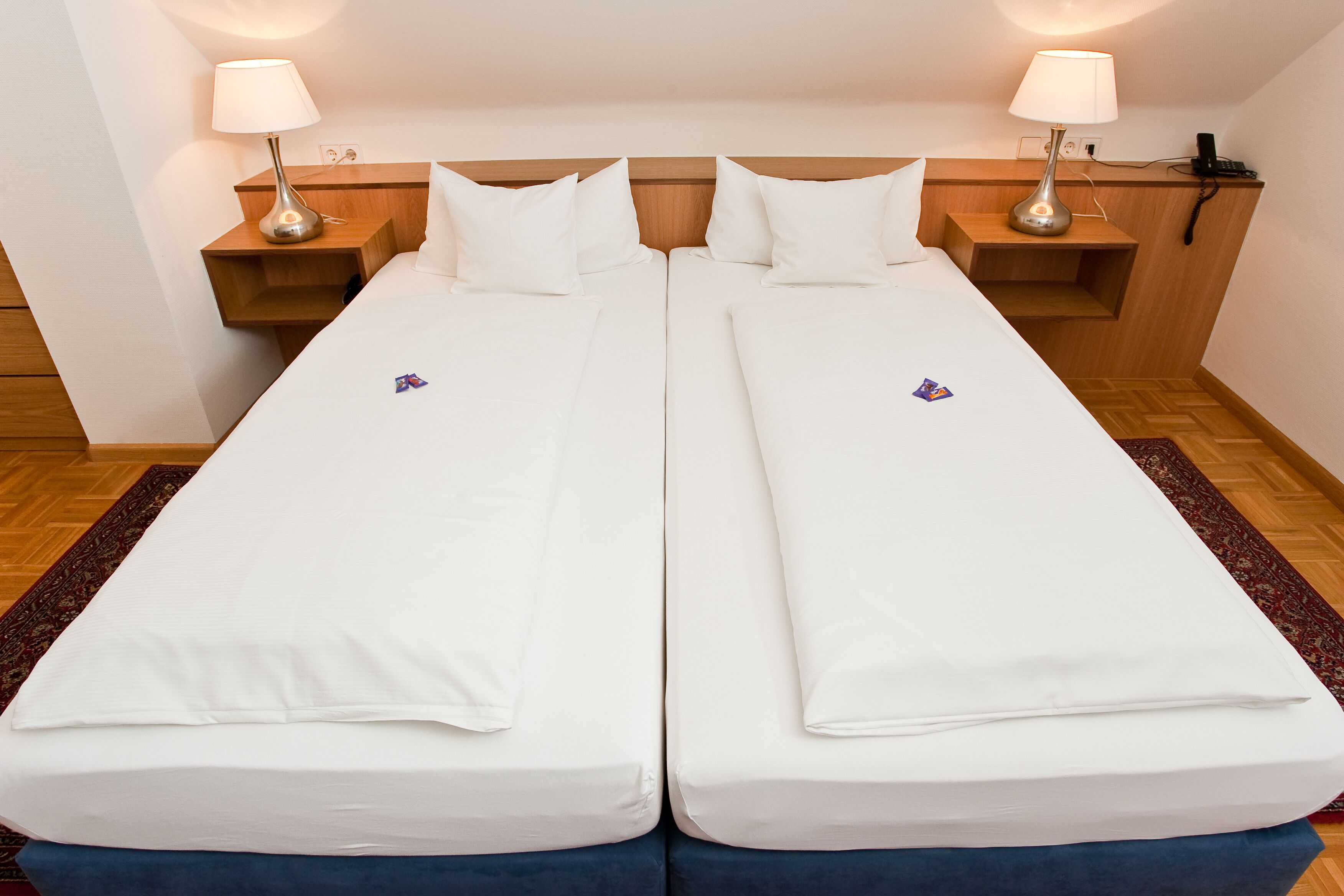 A double bed with white bedding, two bedside tables with lamps, and a wooden headboard.
