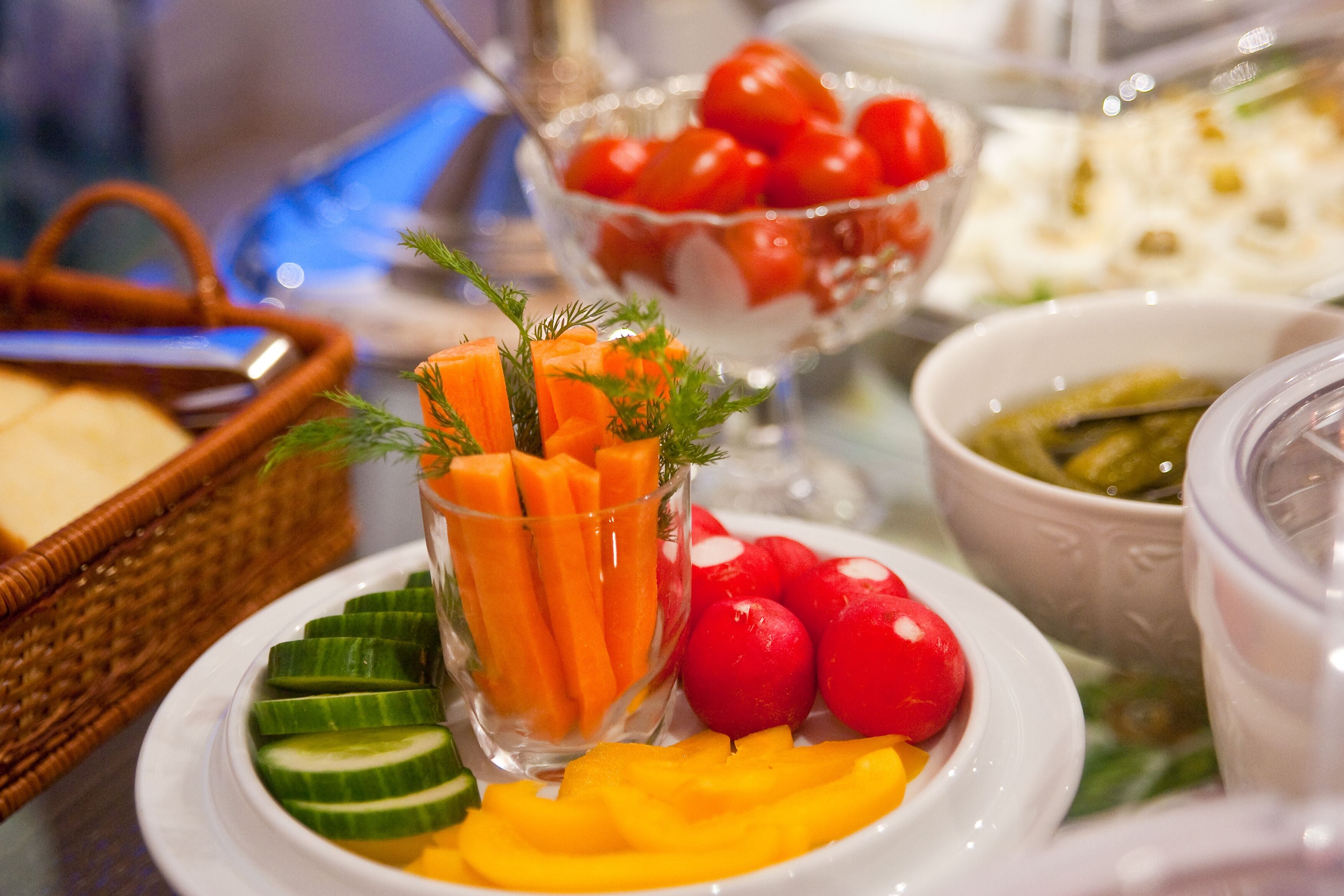 Una mesa con diversos alimentos, como pepinos en rodajas, zanahorias, rábanos y tomates.