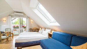 Un dormitorio con tragaluz, una cama, un sofá azul y vistas a un balcón lleno de flores.