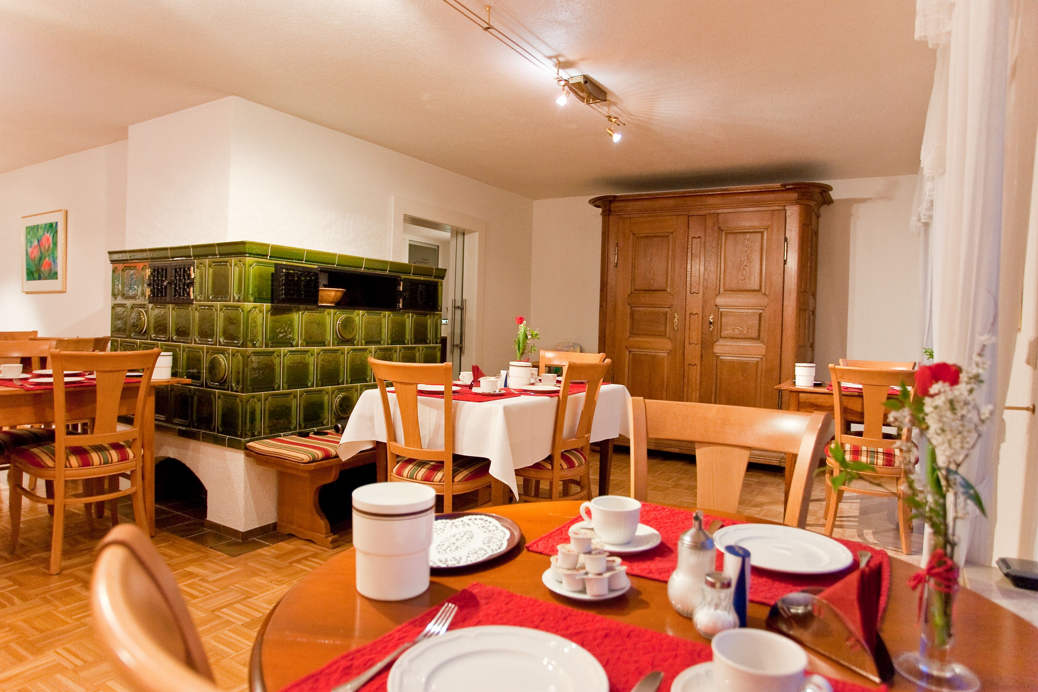 A dining area with wooden tables and chairs, a green tiled backsplash, and a wooden cabinet.