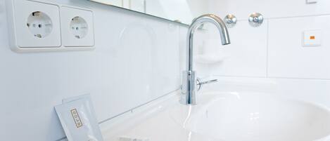 A modern bathroom with a white sink, chrome faucet, and two electrical outlets on the wall.