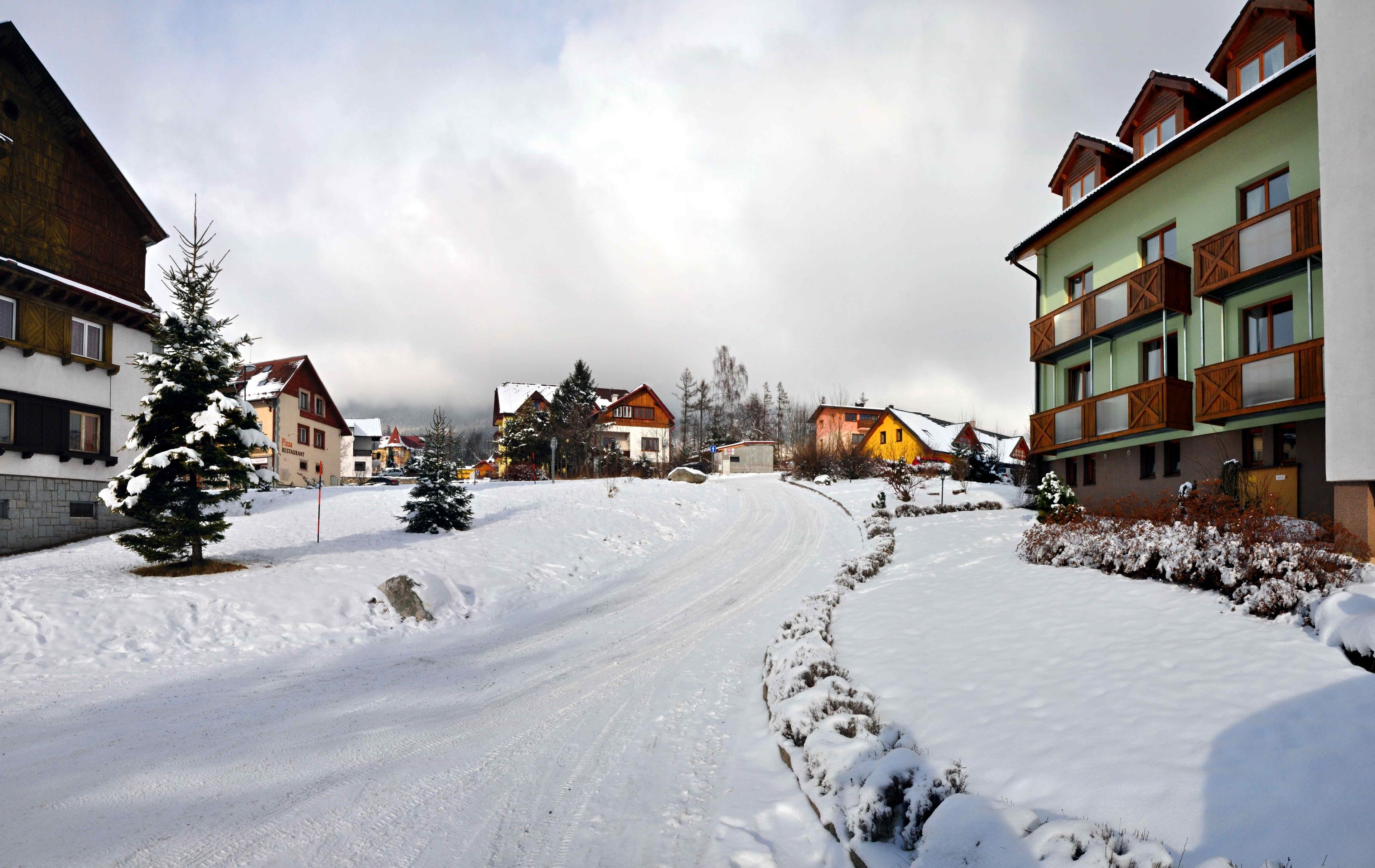 Un pueblo cubierto de nieve con casas de madera tradicionales, un camino despejado y una montaña al fondo.