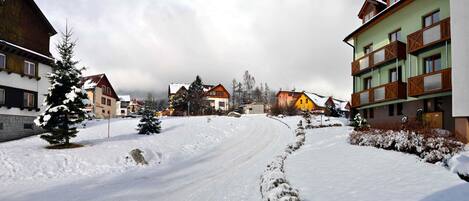 Un pueblo cubierto de nieve con casas de madera tradicionales, un camino despejado y una montaña al fondo.