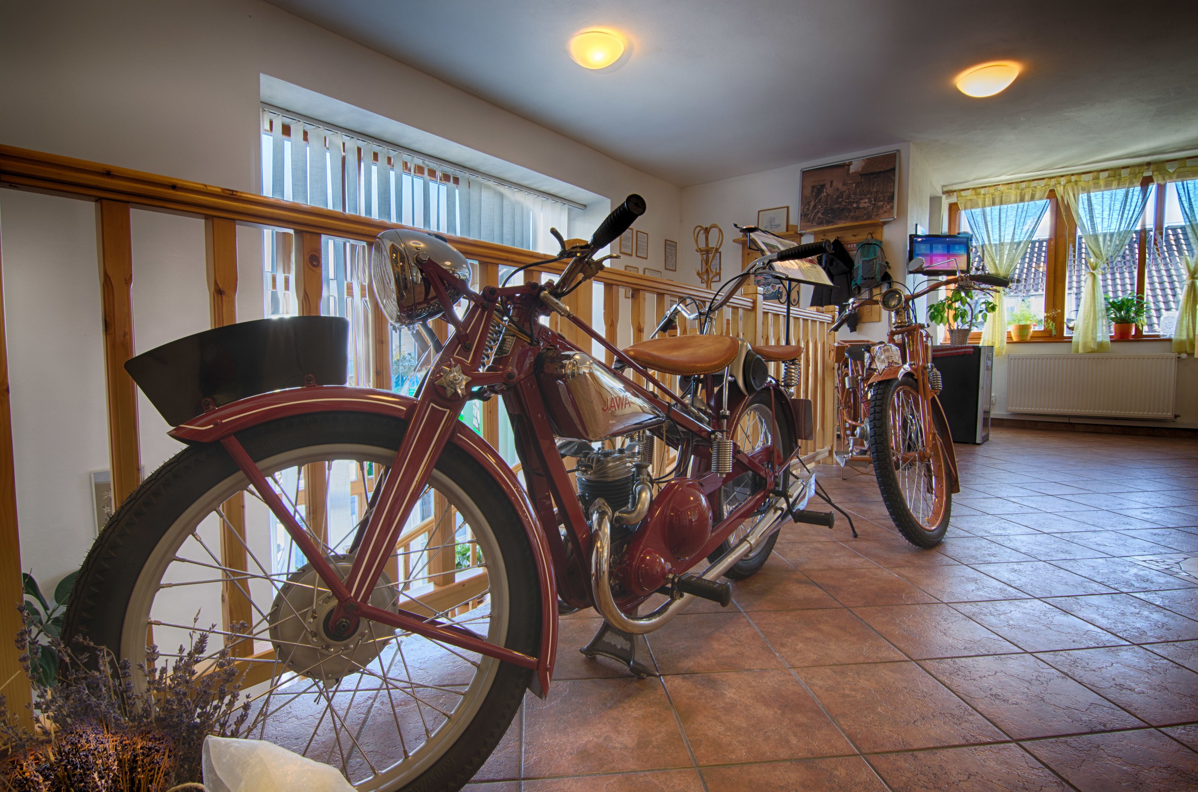 Una habitación con una motocicleta antigua, barandilla de madera y una ventana con cortinas.