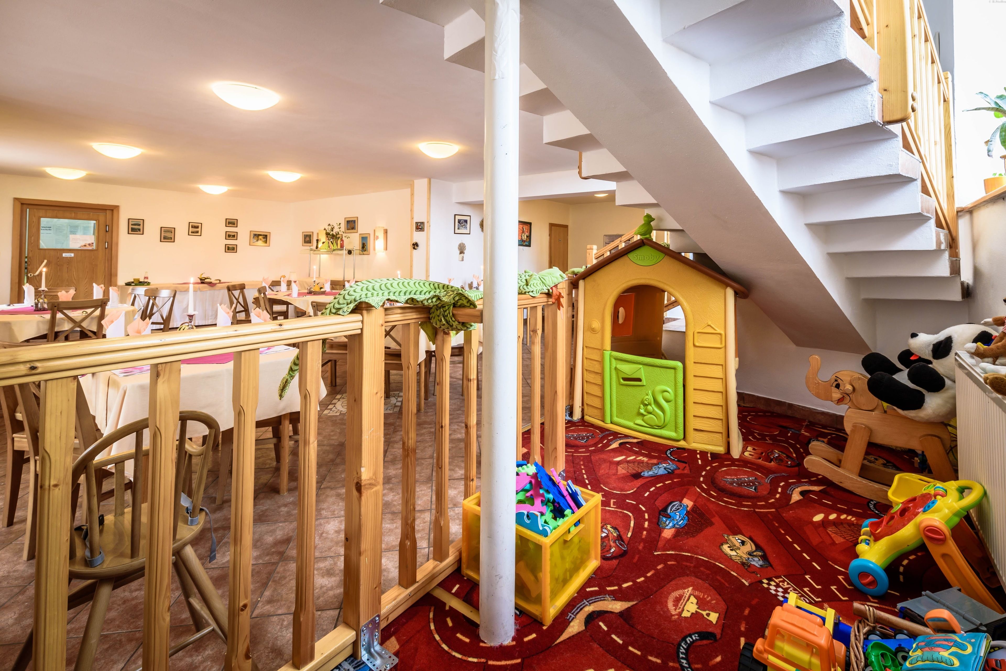 A playroom with a wooden playhouse, a red carpet, and a staircase.