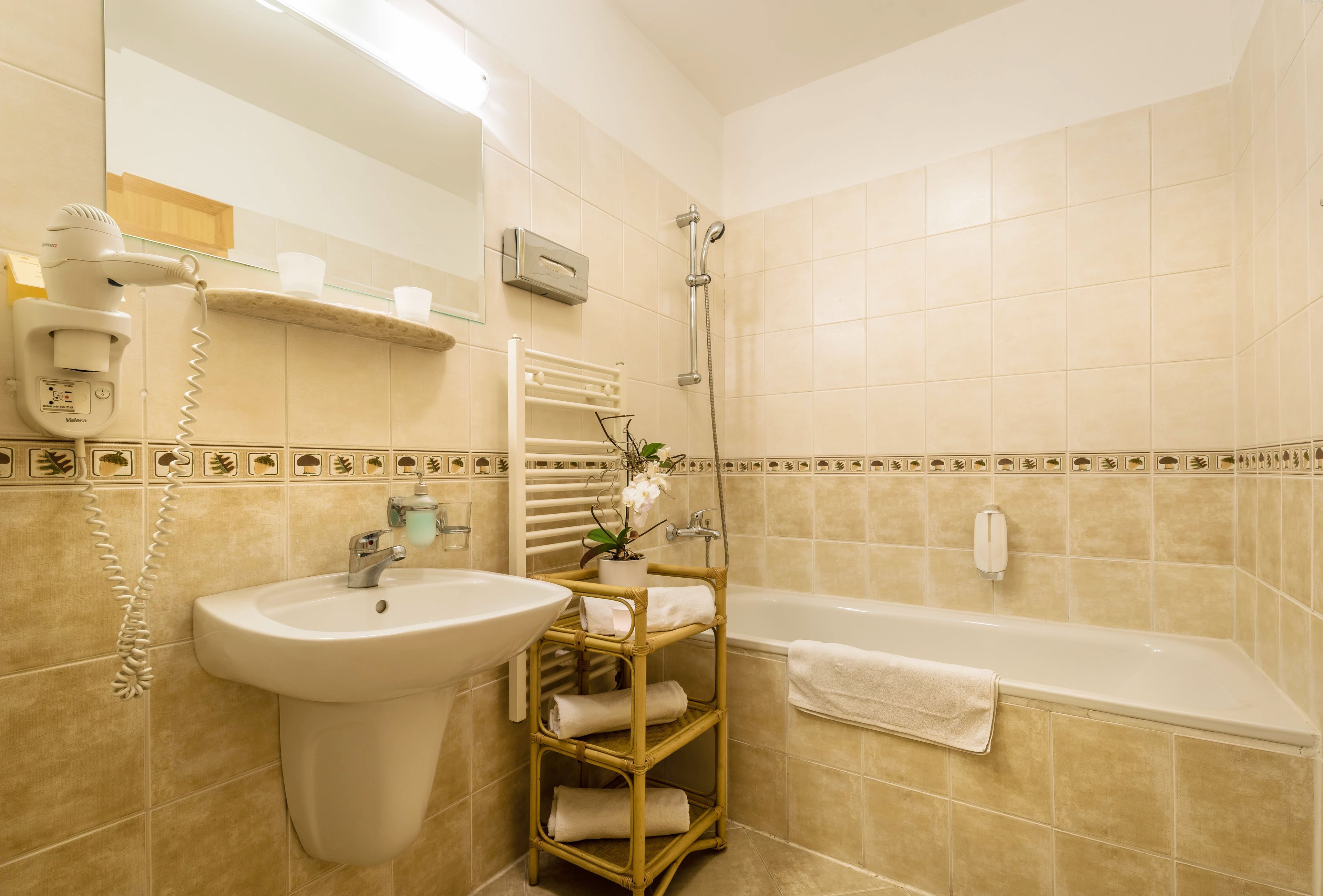 A bathroom with a sink, mirror, hairdryer, shelf with towels, and a bathtub.