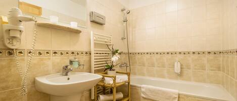 A bathroom with a sink, mirror, hairdryer, shelf with towels, and a bathtub.