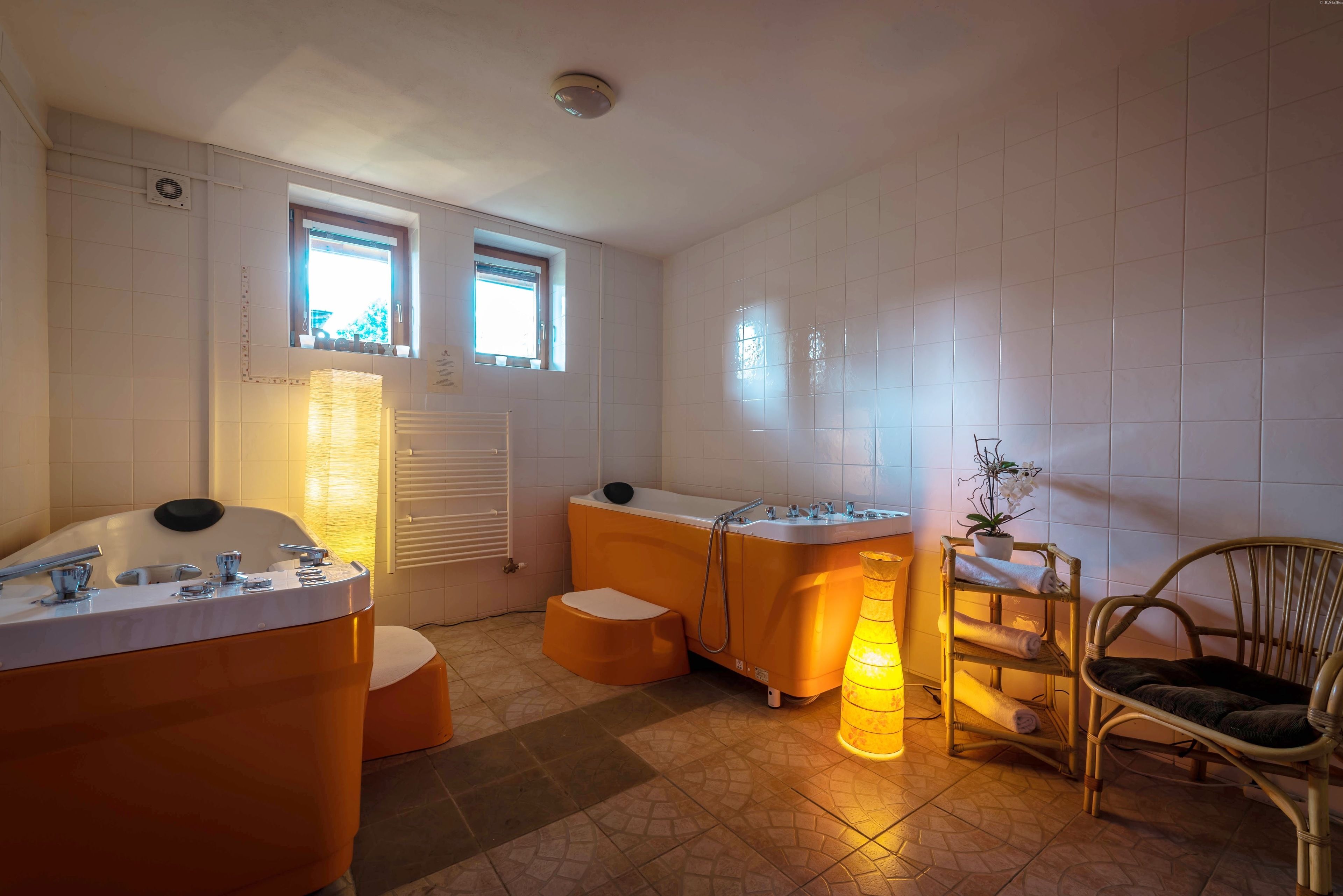 A bathroom with a bathtub, a sink, and a chair. There are two windows providing natural light.