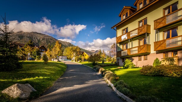 A hotel with a mountain backdrop, a paved driveway, and well-maintained lawns.