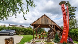 A rustic wooden gazebo with a sloped roof, a wooden swing set, and a red abstract sculpture.