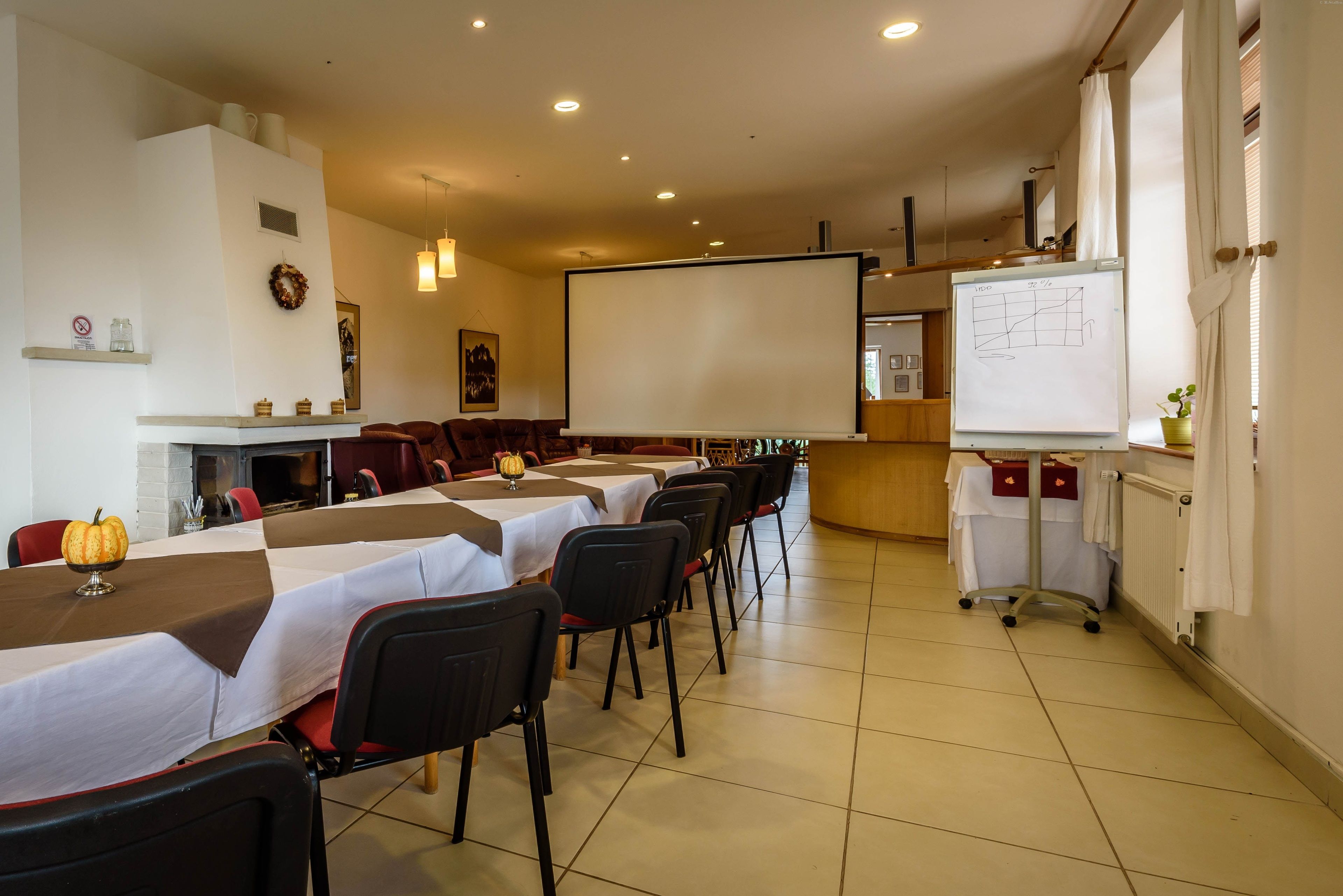 Una sala de conferencias con una larga mesa, sillas, una pizarra y una pantalla para proyector.