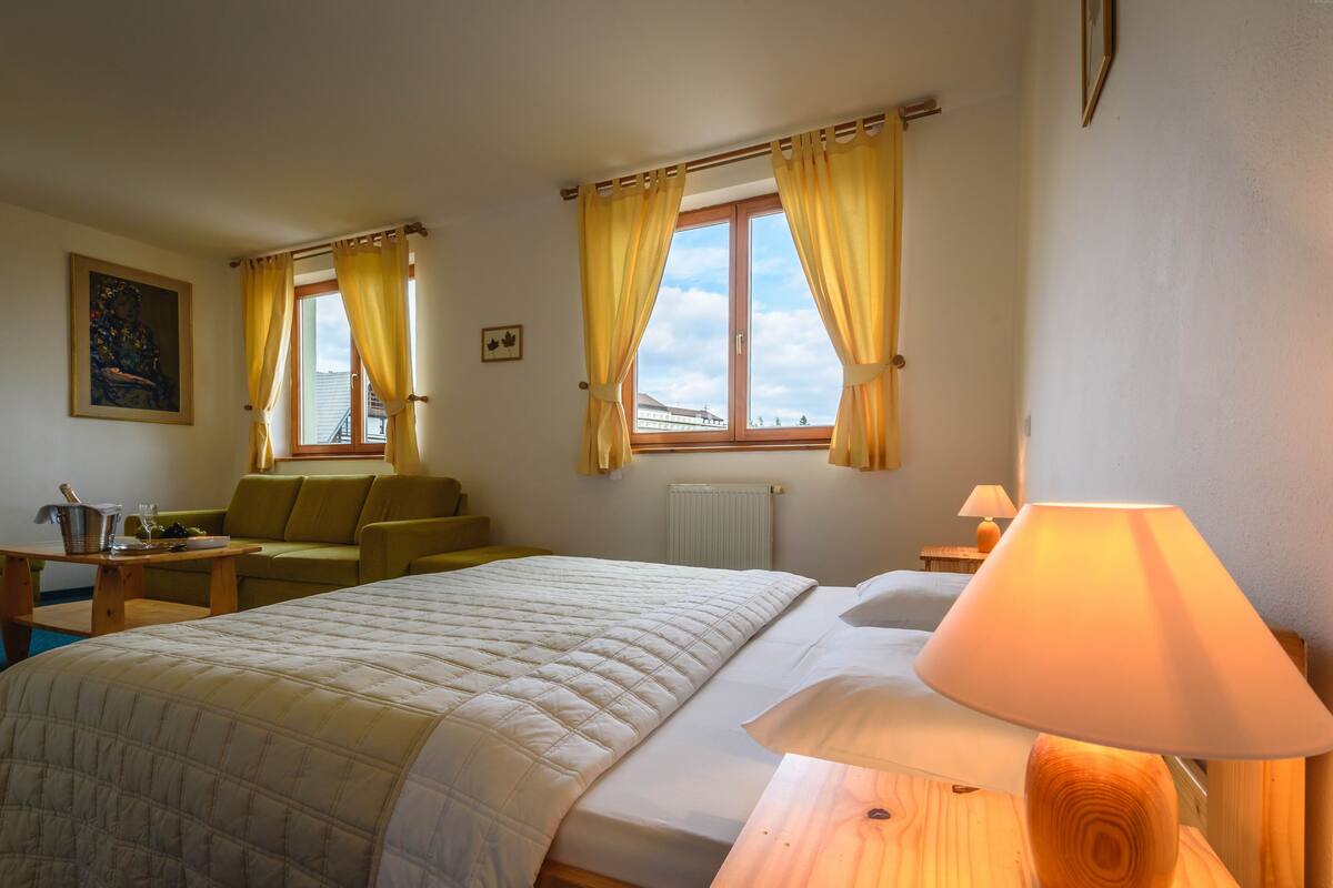 Hotelkamer met een bed, een bank, een tafel met lamp en een raam met gordijnen.