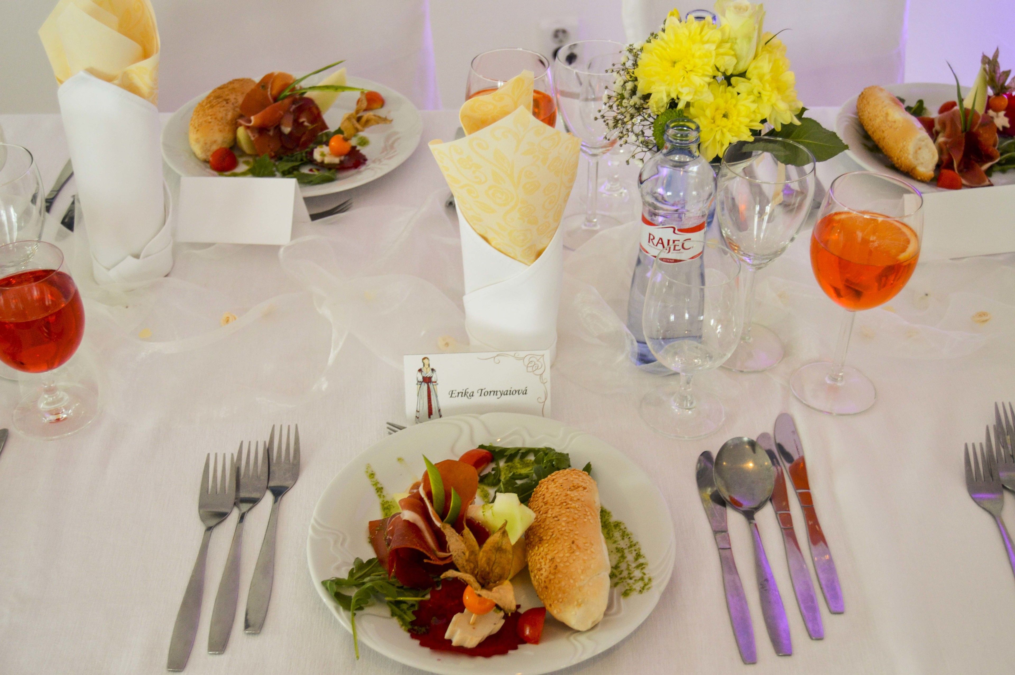 Une table dressée pour un repas, avec des assiettes remplies de nourriture, des couverts, des verres et une bouteille d’eau.