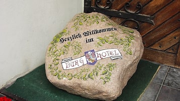 Ein Stein mit Text und einem Logo, auf einer grünen Matte vor einer Holztür platziert.