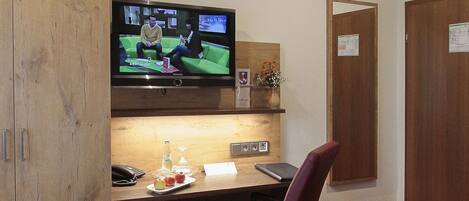 Habitación de hotel con armario de madera, un escritorio con una computadora portátil, televisión y piso cubierto de alfombra roja.