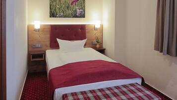 A hotel room with a bed, a bench, a nightstand, a wall-mounted lamp, and a painting.