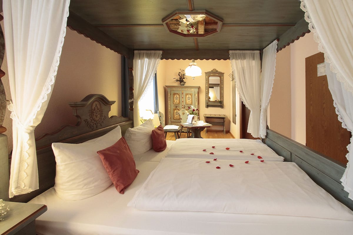 A hotel room with two beds, white bedding, a wooden headboard, a small table with a lamp, and a mirror on the wall.
