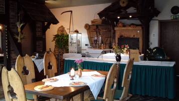 A rustic dining area with wooden chairs and tables, a fireplace, and a green tablecloth.
