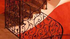 Una escalera en espiral con barandillas de metal negro ornamentadas y una pared roja.