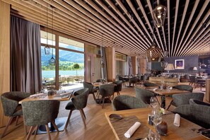 A restaurant with wooden ceiling beams, large windows, and a view of the outdoors. Tables are set with chairs and dining ware.