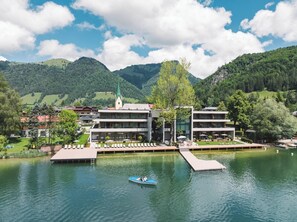 A lakeside hotel with a boat dock, a church, and mountains in the background.