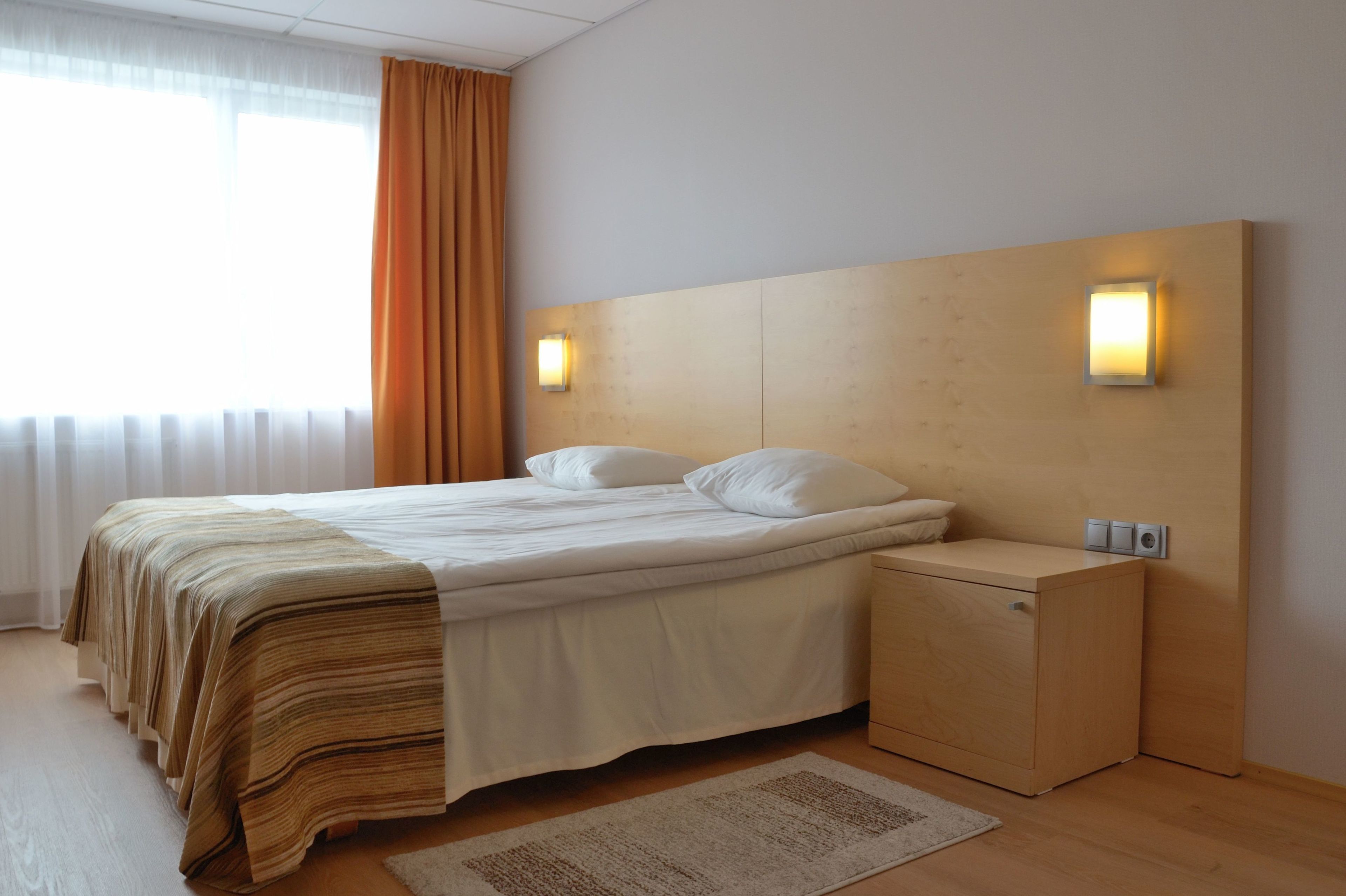 Una habitación de hotel moderna con una cama grande, un cabecero de madera, lámparas de noche y un pequeño mueble de madera.