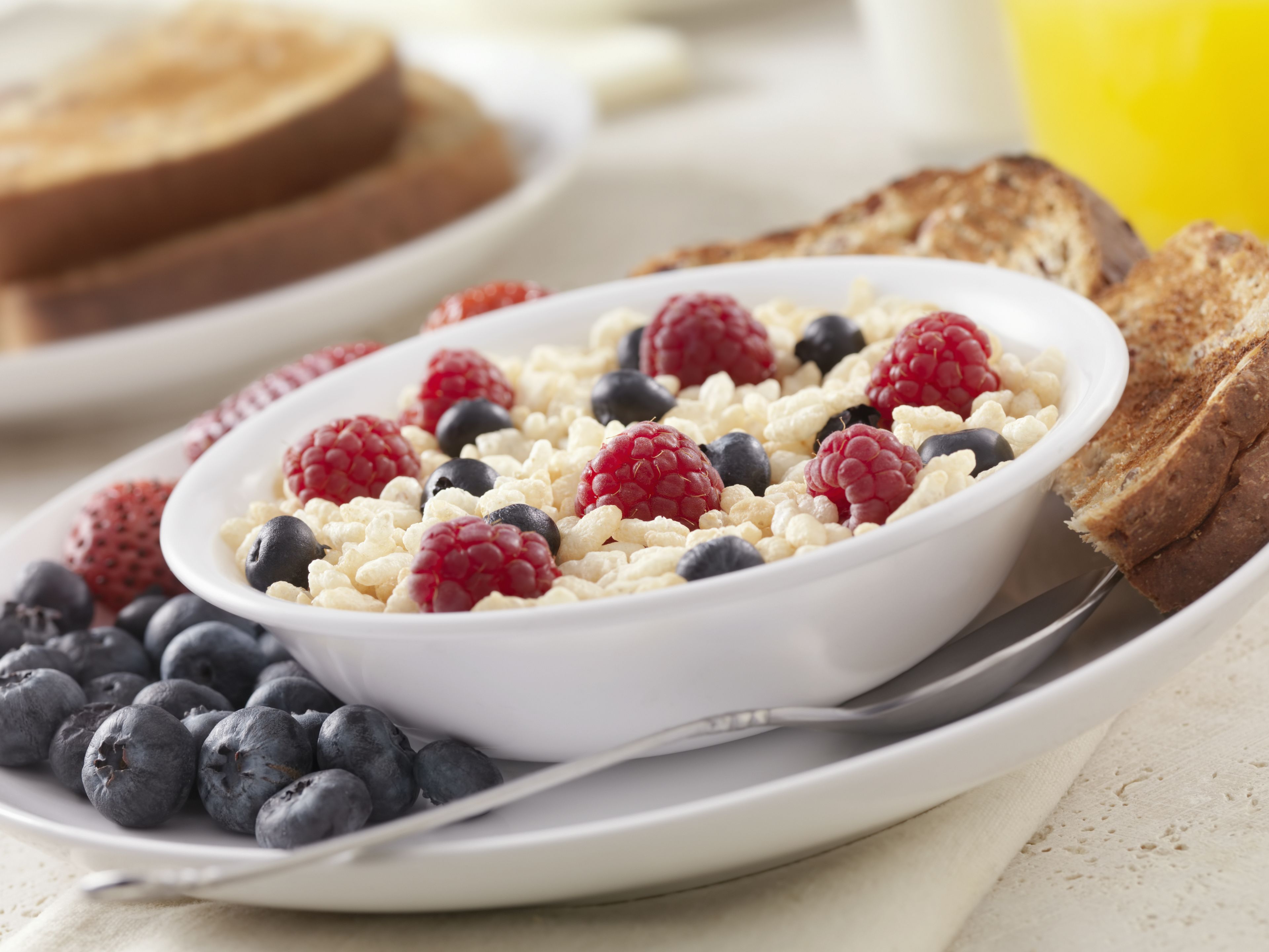 A bowl of cereal with berries and toast on a plate.