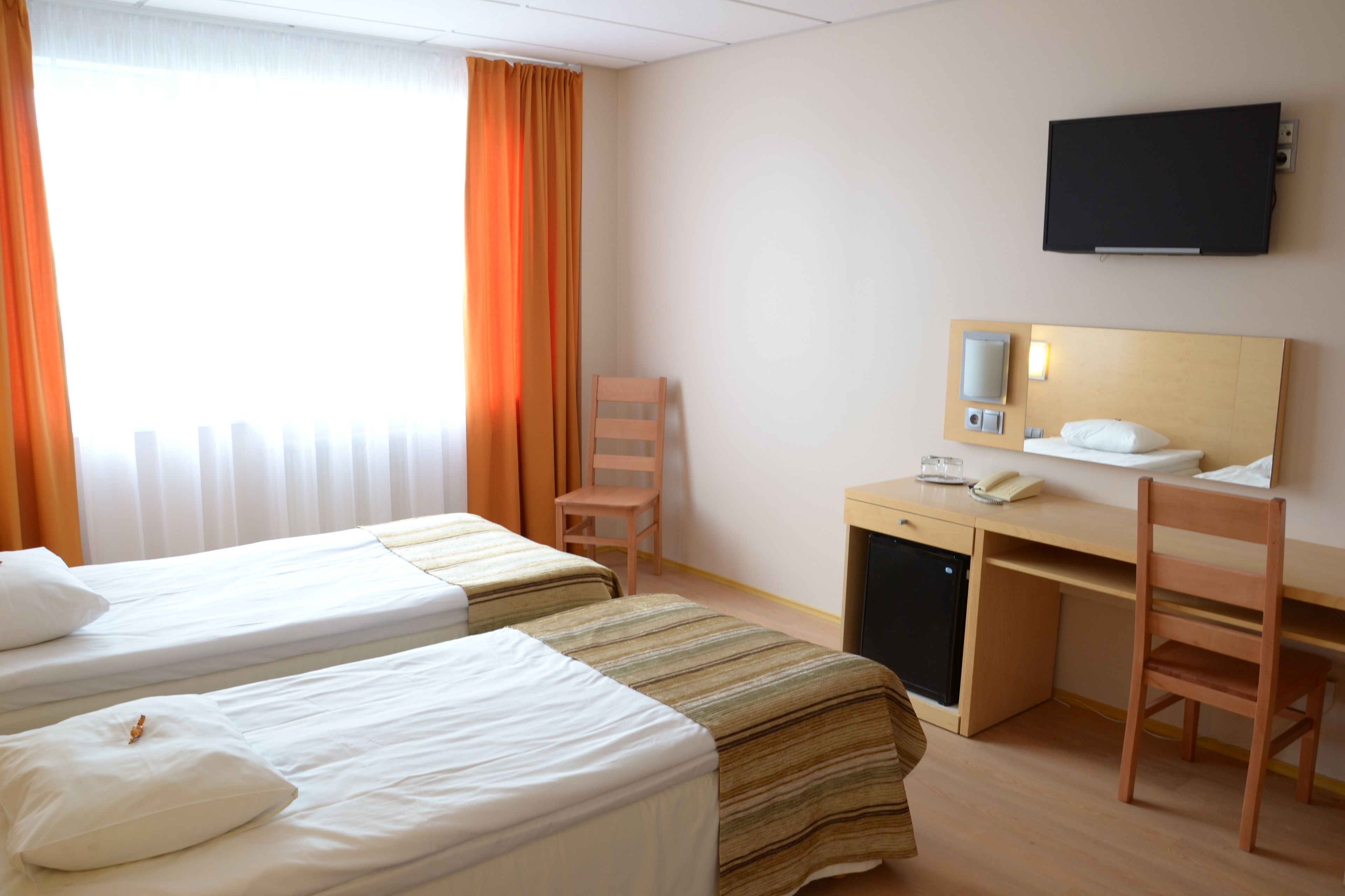 A hotel room with two beds, a desk, a chair, a television, and a window with curtains.