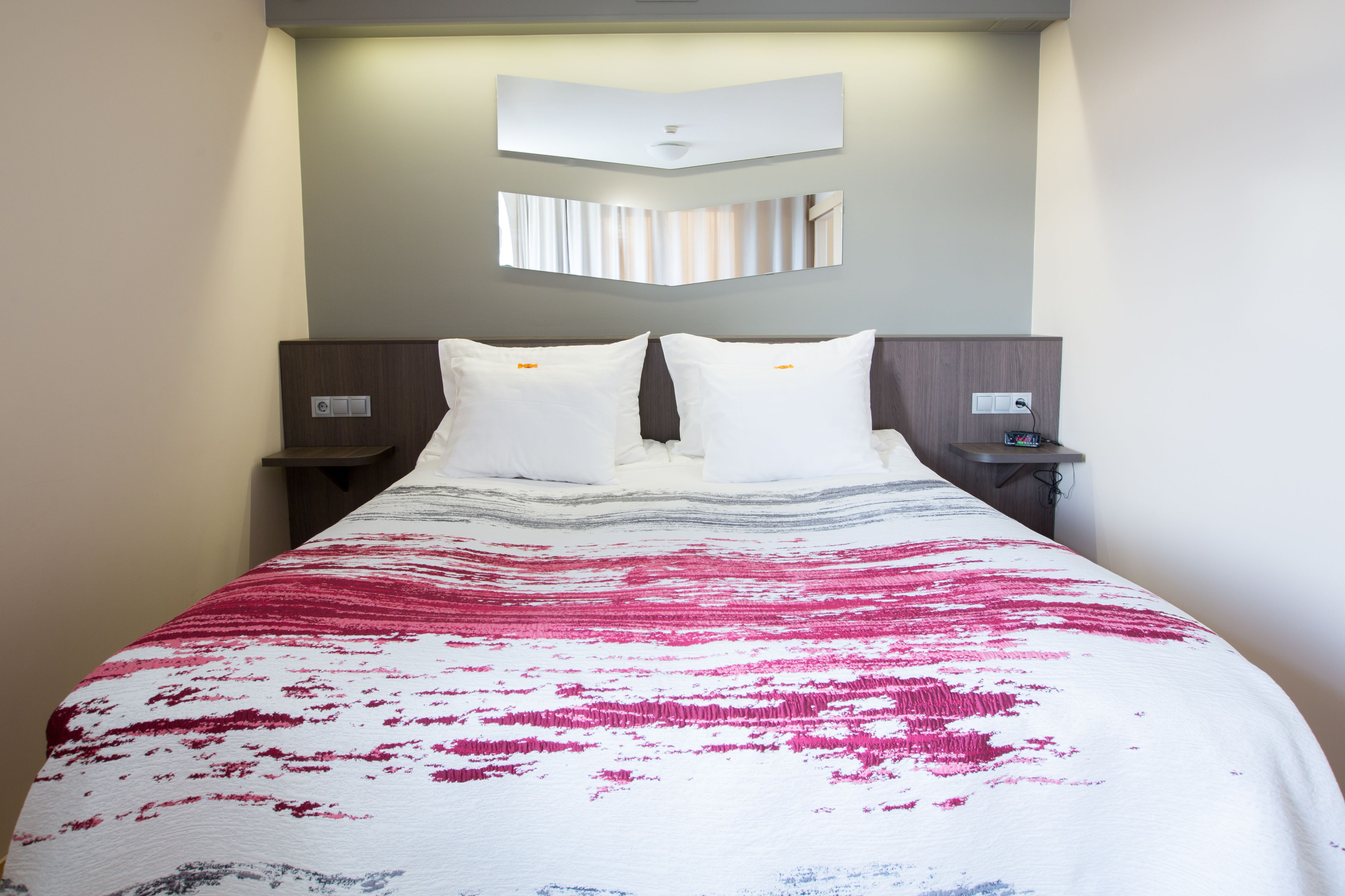 A hotel room with a large bed, two bedside tables, a wall-mounted mirror, and a ceiling light fixture.