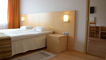 A hotel room with a bed, bedside tables, a nightstand, a wall-mounted TV, and a wooden floor.