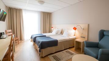 A hotel room with two beds, a desk with a chair, a TV, and a blue armchair.