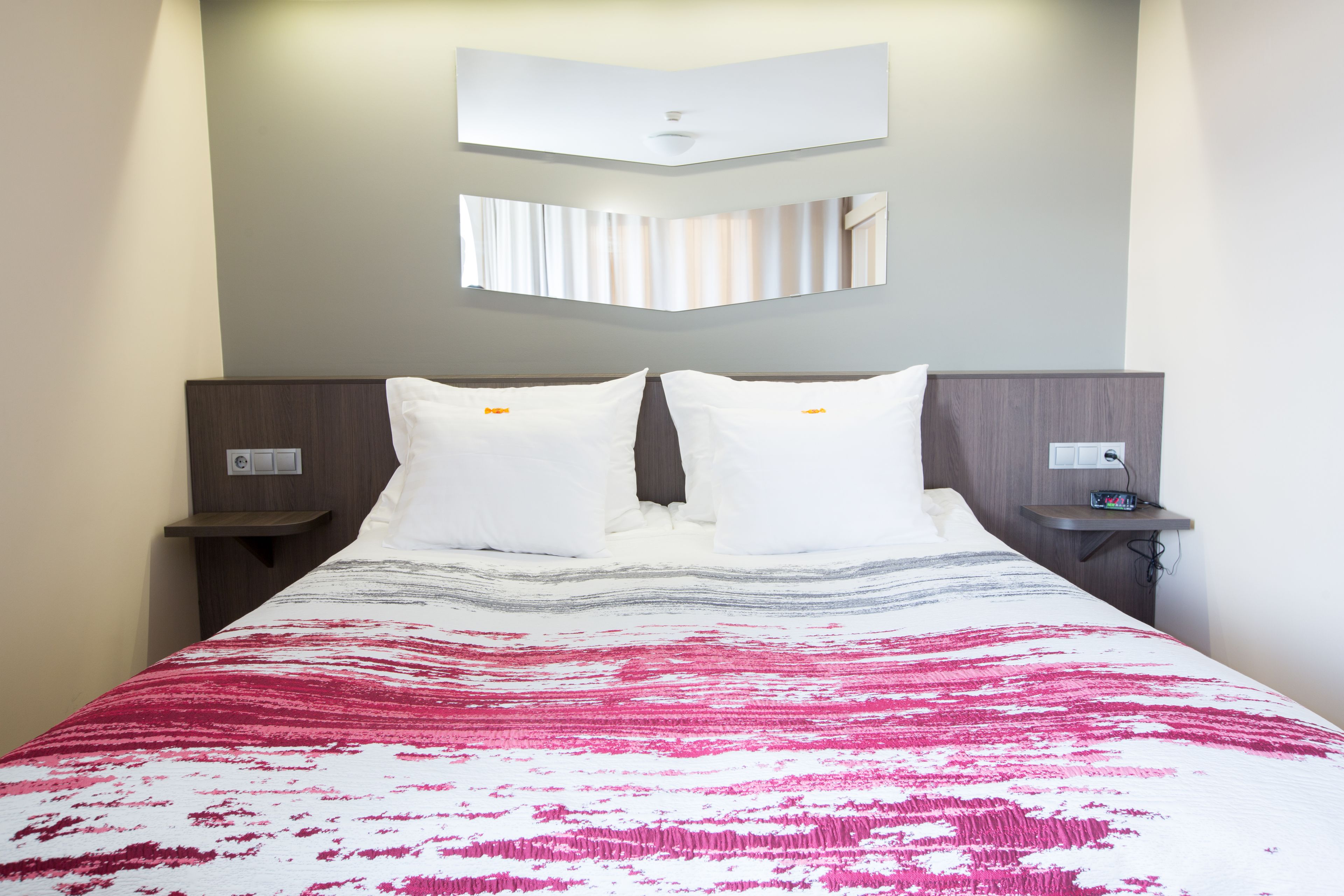 A hotel room with a bed, two bedside tables, a wall-mounted TV, and a power outlet on the nightstand.