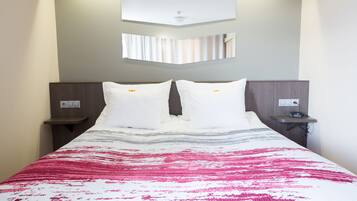 A hotel room with a bed, two bedside tables, a wall-mounted TV, and a power outlet on the nightstand.