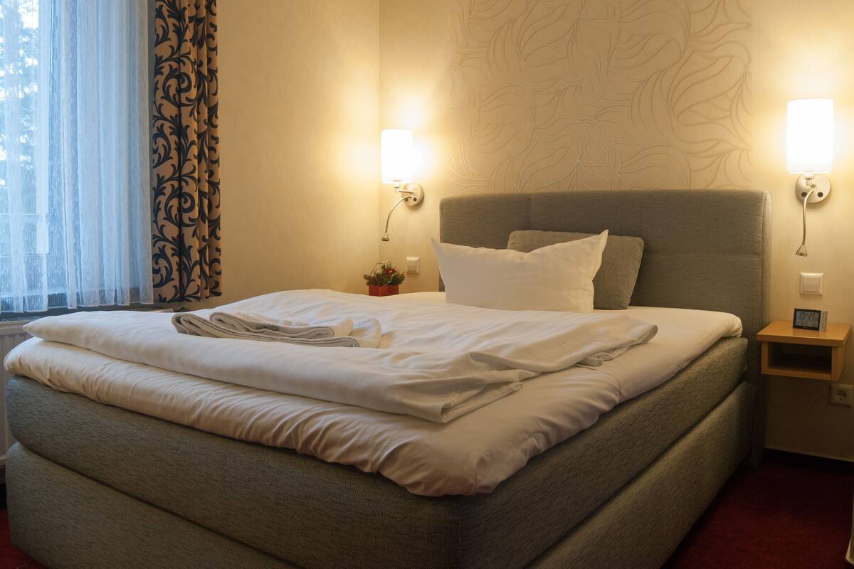 A neatly made bed with white linens, a grey headboard, and two bedside lamps.