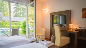 Ein Hotelzimmer mit zwei Betten, einem Schreibtisch, einem Fernseher und Blick ins Freie.