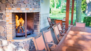 Ein Kamin aus Stein mit Feuer, umgeben von Holzstühlen und einem Tisch auf einer Terrasses.