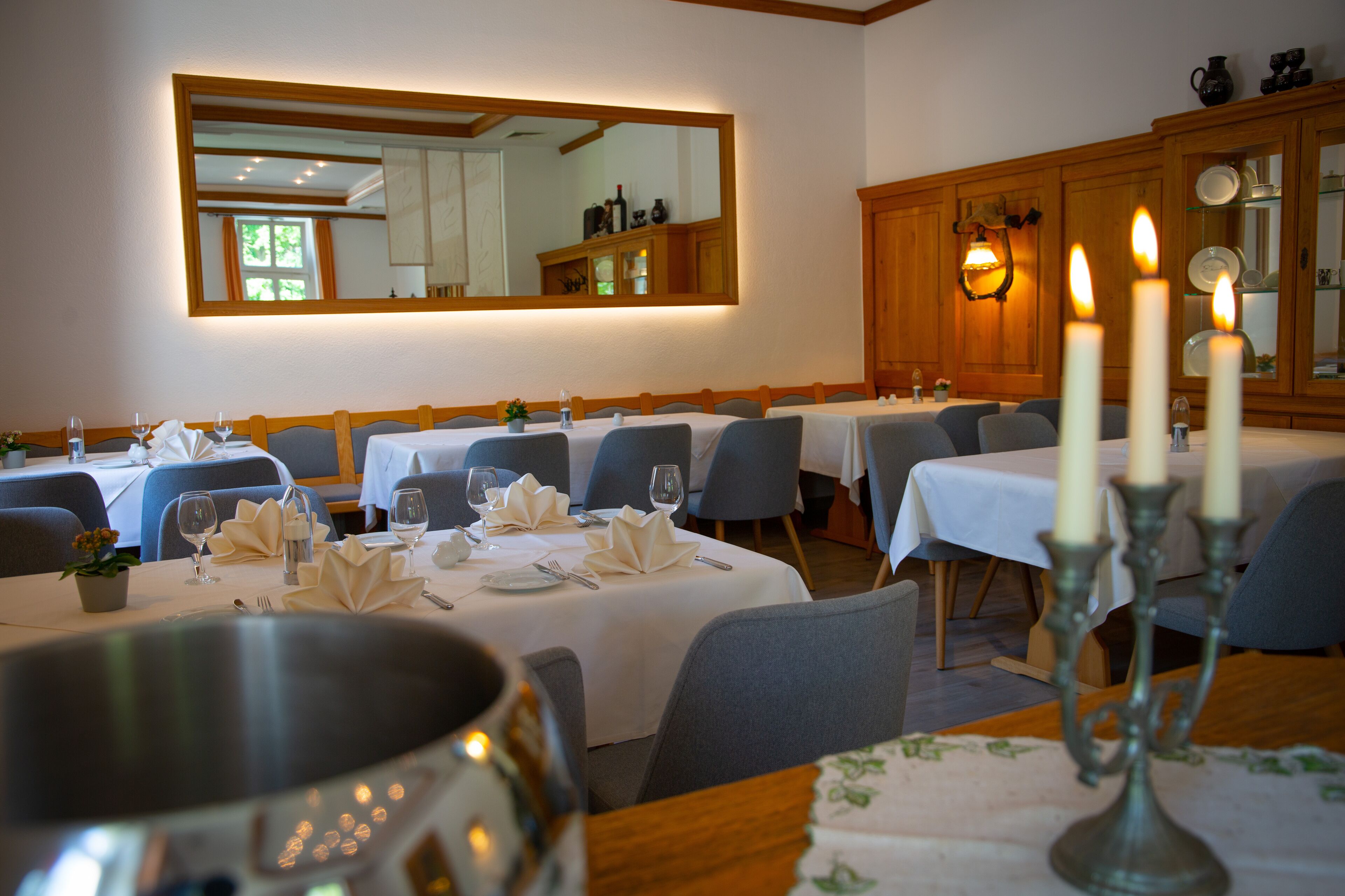 Un comedor con mesas dispuestas para una comida, un espejo grande en la pared y un candelabro con velas.
