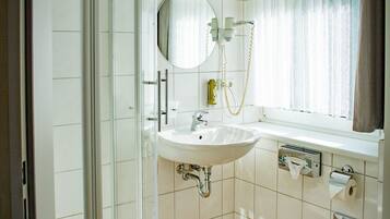 A bathroom with a glass shower enclosure, a sink, a mirror, a toilet, and a window with curtains.