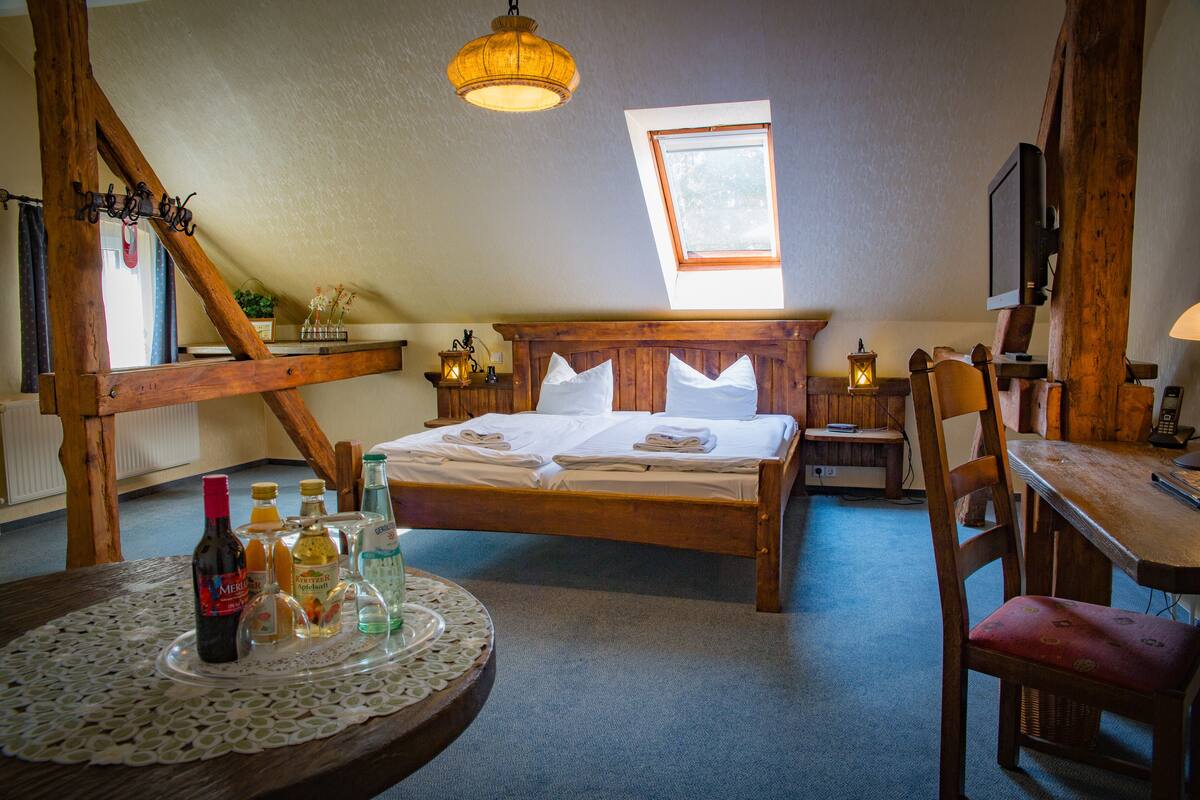 A cozy bedroom with a wooden bed, a round table with drinks, and a window providing natural light.