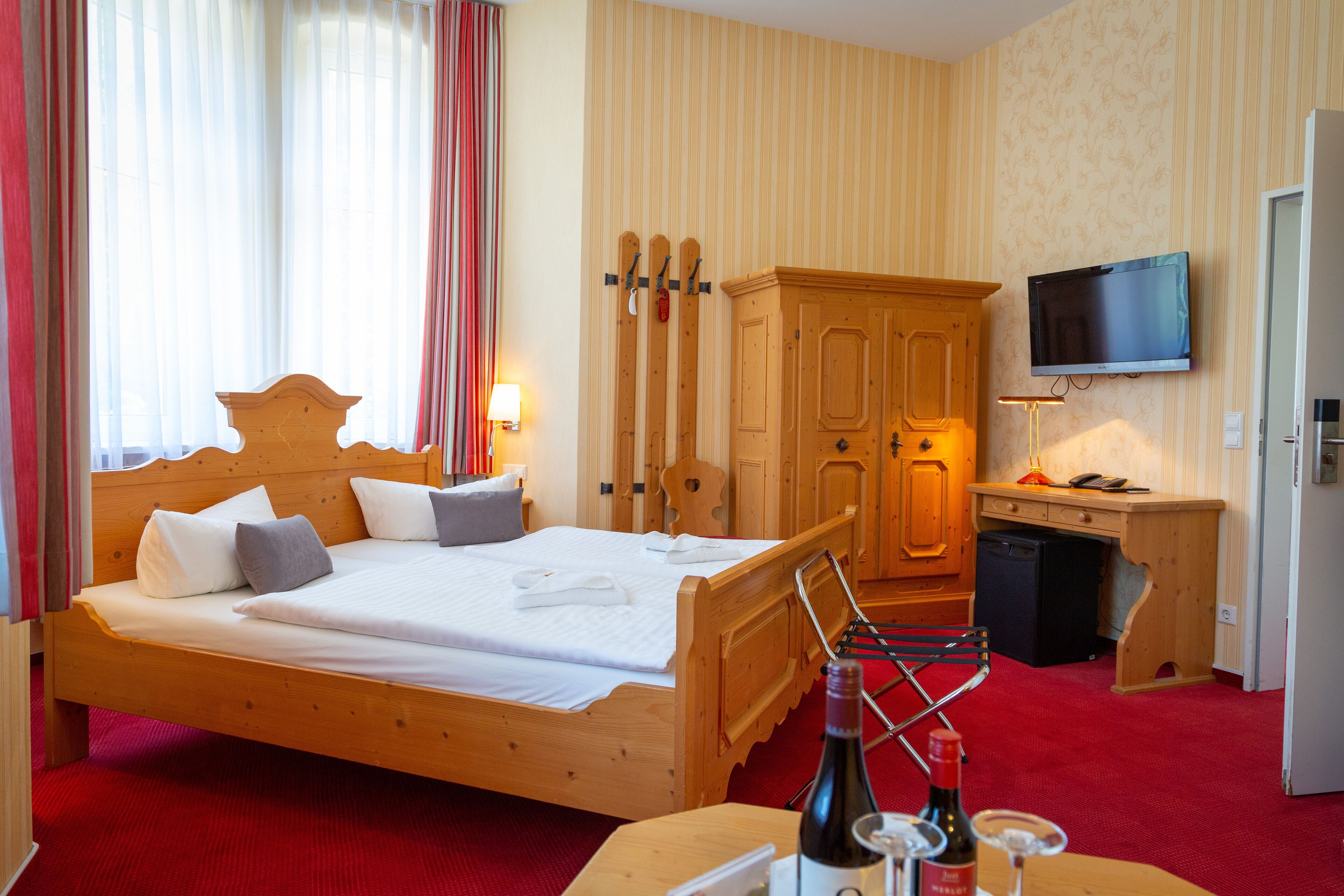 Une chambre d’hôtel avec un lit en bois, un téléviseur fixé au mur et une armoire en bois.