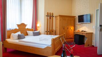Une chambre d’hôtel avec un lit en bois, un téléviseur fixé au mur et une armoire en bois.