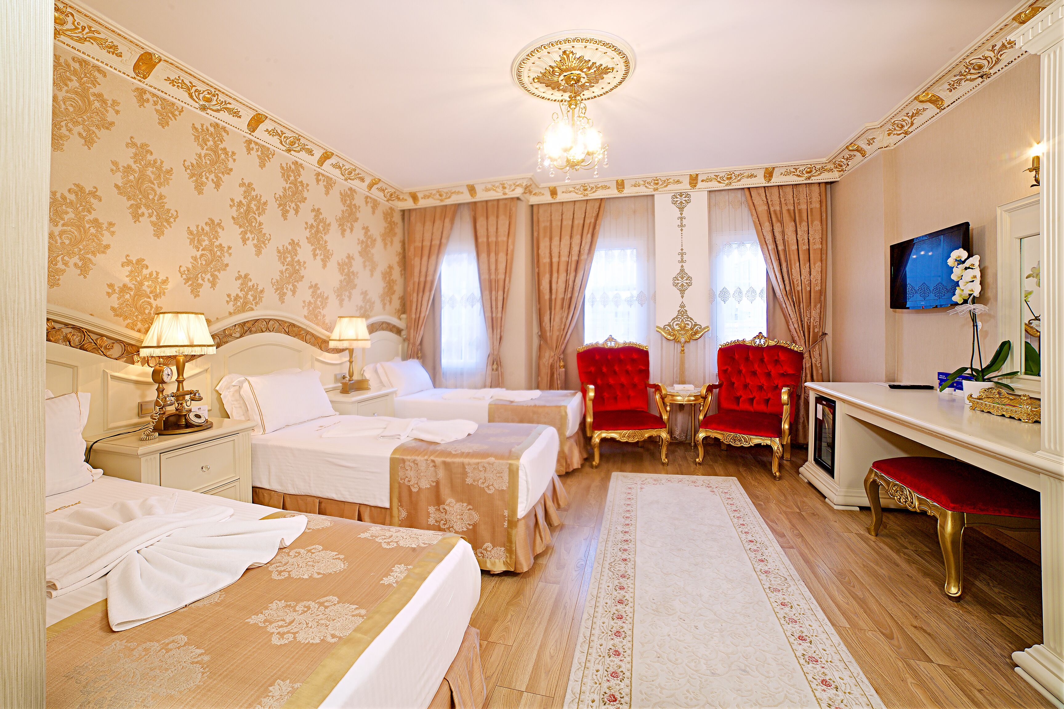 A hotel room with two beds, a desk, a TV, and a red chair.
