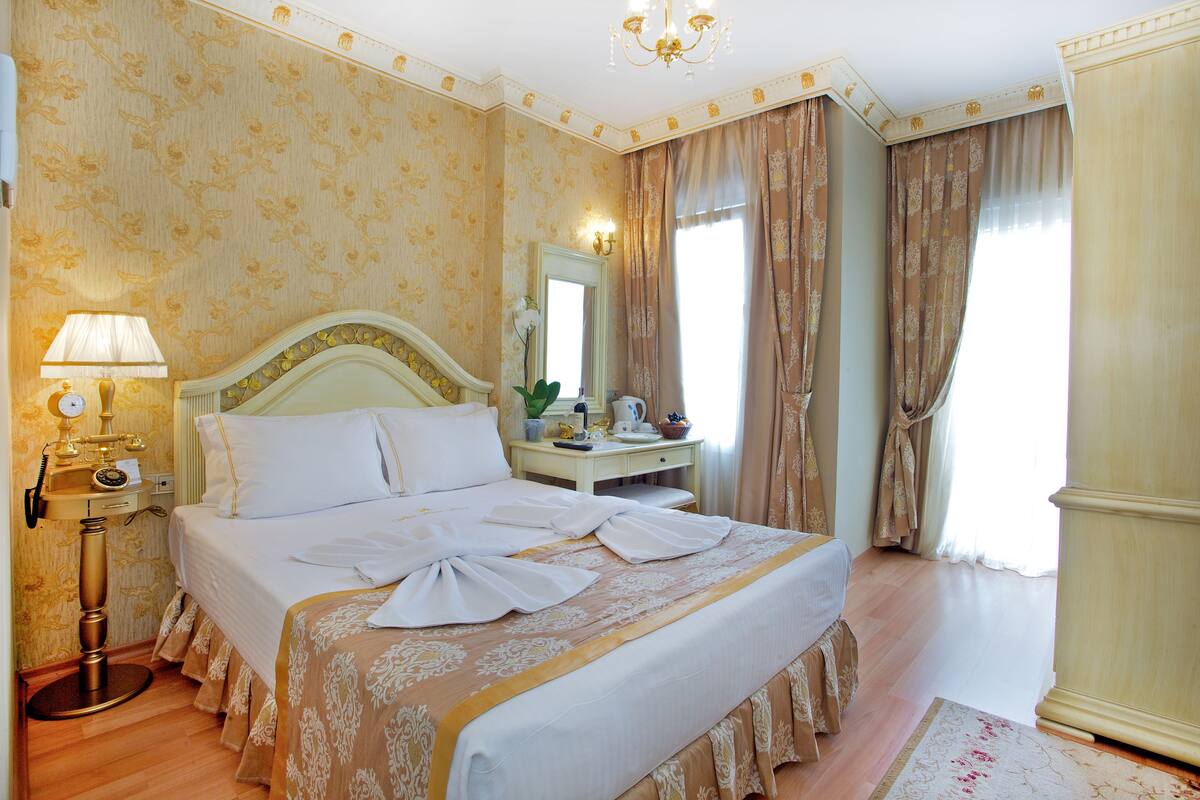 Ein Hotelzimmer mit einem großen Bett, einem Nachttisch, einer Lampe, einem Spiegel und Vorhängen.