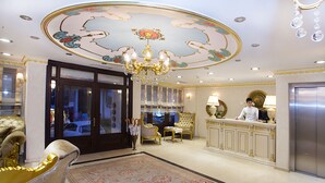Eine luxuriöse Lobby mit aufwendiger Deckenmalerei, einem prunkvollen Kronleuchter, komfortablen Sitzgelegenheiten und einer Rezeption.