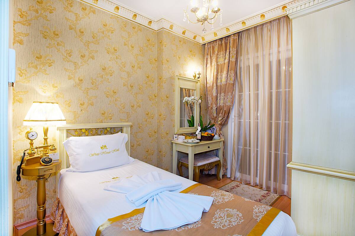 Ein Hotelzimmer mit einem ordentlich bezogenen Bett, einem Nachttisch mit Lampe, einem Spiegel und einem kleinen Schreibtisch mit Stuhl.