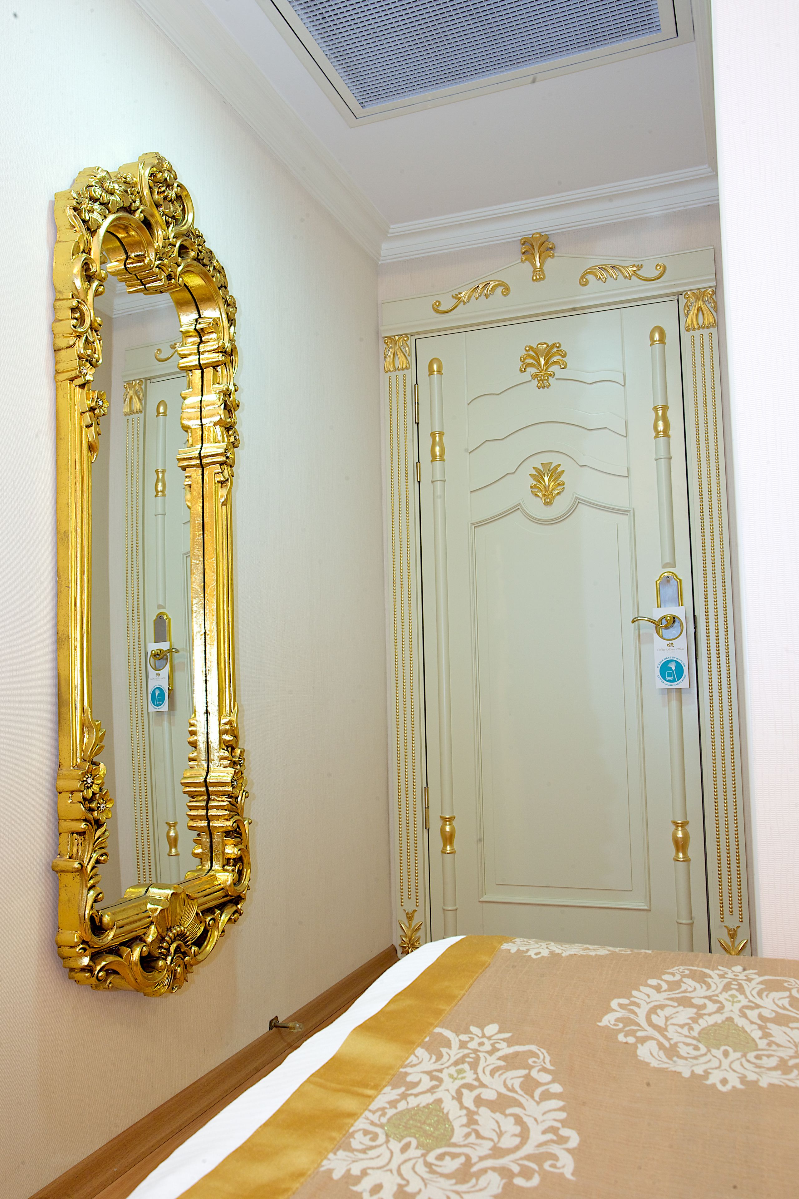 A room with a large ornate mirror, a door with a lock, and a bed with a patterned bedspread.