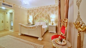 Ein Schlafzimmer mit einem großen Bett, Nachttischen, einem Schminktisch mit Spiegel und einem roten Sessel.